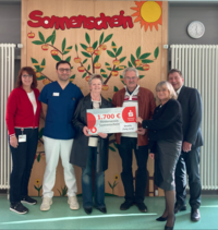 Sechs Personen stehen vor einem Baum-Motiv mit Äpfeln. Eine Person hält ein Schild mit '1.700 €' und 'Sonderverein Sonnenschein'.