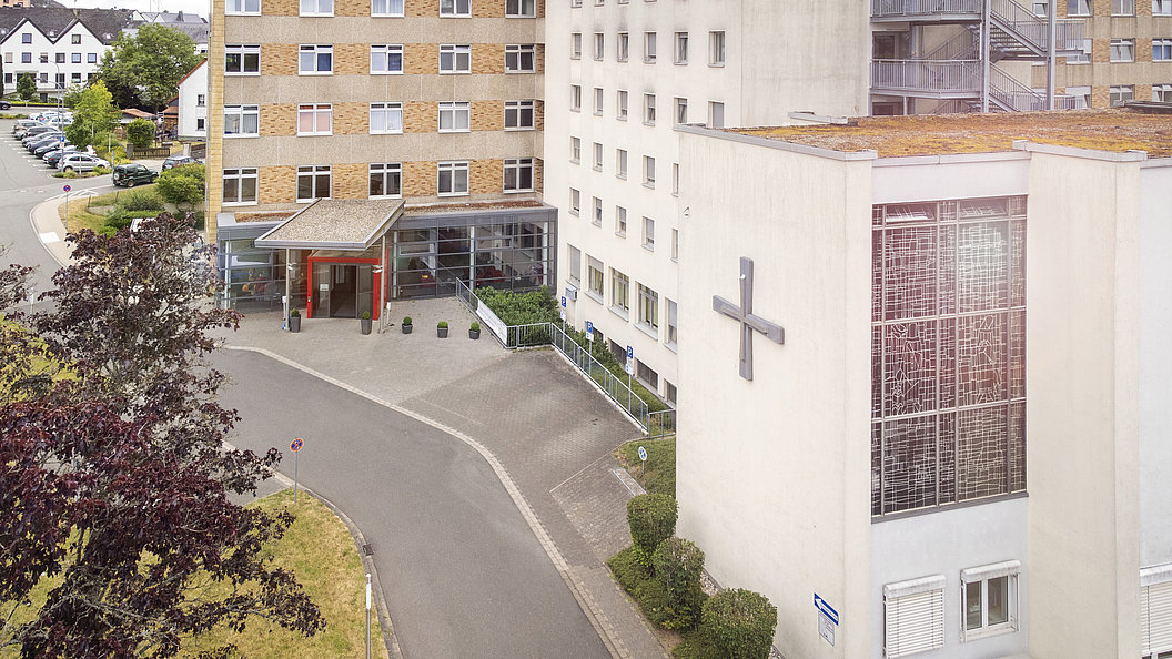 Außenansicht des Marienhaus Klinikums Eifel mit Eingangsbereich und großem Kreuz an der Fassade.