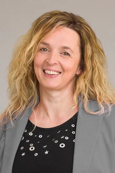 Bianca Nonweiler mit langen, lockigen blonden Haaren, grauem Blazer und schwarzem Shirt mit weißem Muster.