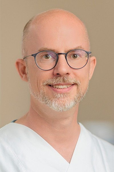 Porträt eines Mannes mit Glatze und weißem Hemd vor neutralem Hintergrund