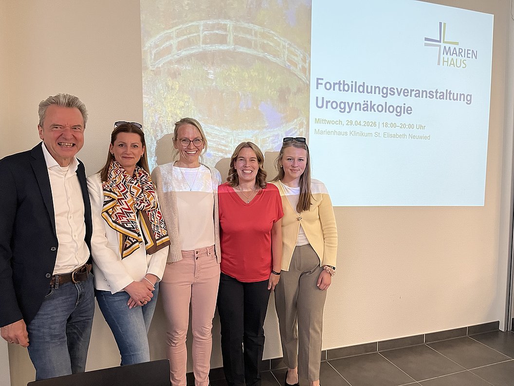 Fünf Personen stehen nebeneinander vor einer Wand mit einem Projektionsbild zur Fortbildungsveranstaltung Urogynäkologie im Marienhaus.