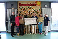 Gruppe von sieben Personen steht in einem Raum vor einer Wand mit einem großen bunten Wandbild mit der Aufschrift 'Sonnenschein' und hält einen großen symbolischen Scheck