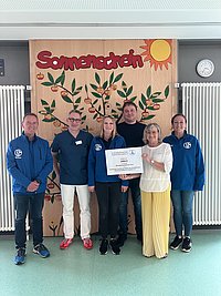 Sechs Personen stehen vor einer Wand mit einem großen Poster, das eine Pflanze und die Aufschrift 'Sonnenschein' zeigt, zwei Personen halten ein großes Schild