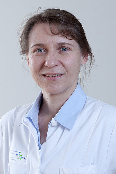 Elisabeth Bergmann, Oberärztin und Fachärztin für Anästhesiologie, trägt einen weißen Arztkittel und lächelt in die Kamera