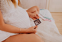 Schwangere Frau sitzt auf einem Bett und hält ein Ultraschallbild in den Händen