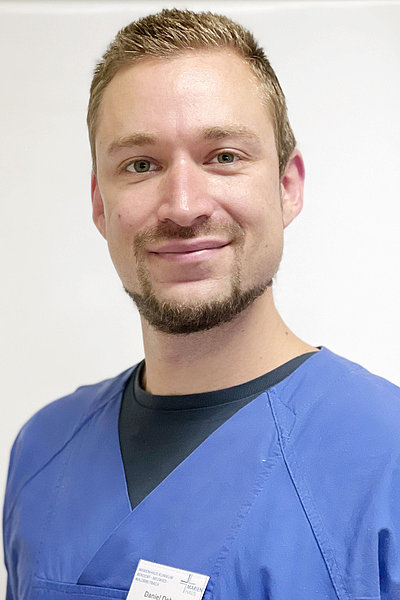Daniel Dehnert, Leiter der Station 12 Intensivstation, in blauer medizinischer Arbeitskleidung, lächelnd