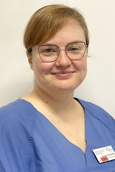 Annika Zühlke, stellvertretende Leitung Station 12, trägt blaue Arbeitskleidung und eine Brille, lächelt leicht