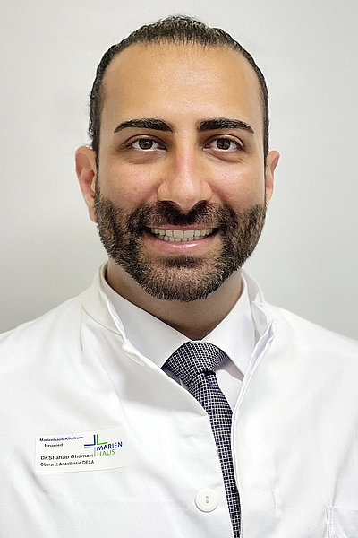 Dr. Shahab Ghamari, Oberarzt und Facharzt für Anästhesiologie, lächelnd in weißem Arztkittel mit Krawatte