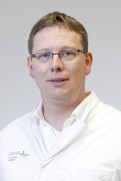 Dr. Martin Reuber, Oberarzt und Facharzt für Anästhesiologie, trägt weiße Arztkleidung und Brille