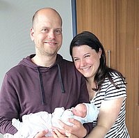Zwei Erwachsene halten gemeinsam ein schlafendes Baby in weißen Kleidern